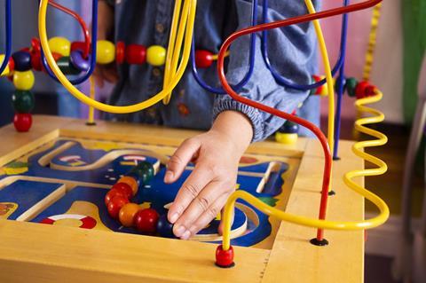 A child's hand playing with a toy which includes beads that need to be pushed along wavy shaped wire paths.