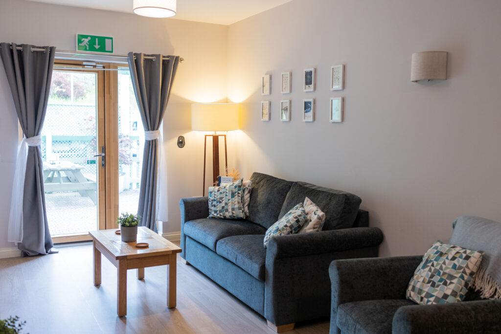 The lounge area if the Snowflake Suite, with a large comfortable sofa and chair leading to a patio door with a small outdoor area beyond.