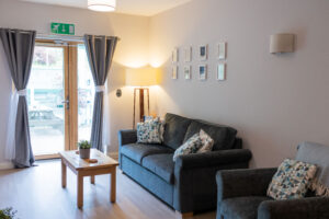 The lounge area if the Snowflake Suite, with a large comfortable sofa and chair leading to a patio door with a small outdoor area beyond.