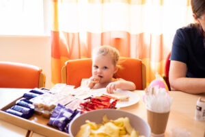 A young while girl with blonde hair sat at a table and eating a sandwich from a plate