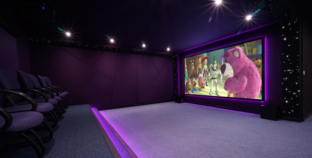 The cinema room at Russell House in low light, illuminated by purple strip lights and sparkling star lights on the wall. Toy Story is playing on the screen.