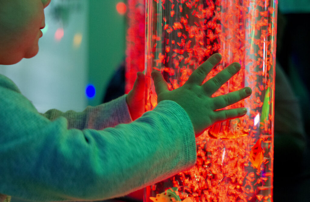 A bubble light tube glowing red in the sensory room, with a small child's hands holding the tube.