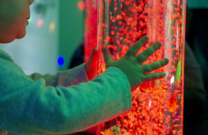 A bubble light tube glowing red in the sensory room, with a small child's hands holding the tube.