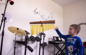 A small boy in the music therapy room, surrounded by different instruments, as he reaches out towards a set of metal chimes.