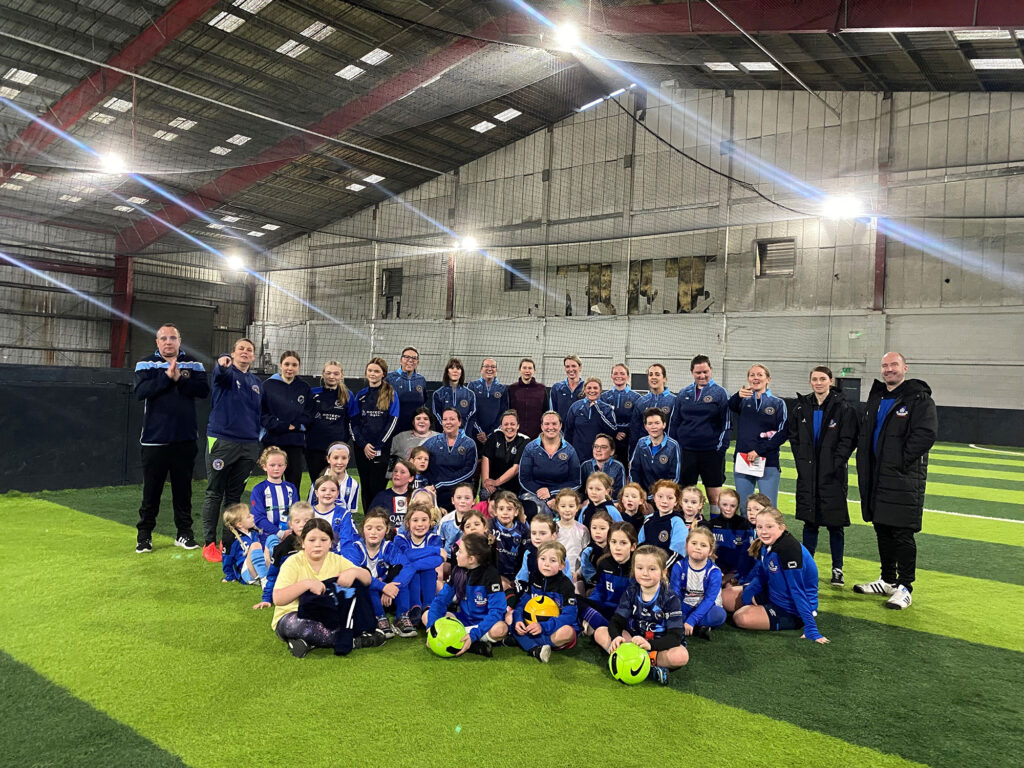 A large group of students and teachers from Shelley college in sports uniforms inside an indoor football pitch.