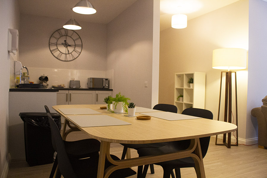 The kitchen area of the Snowflake Suite at Russell House, showing a modern dining table and a small kitchenette with soft lighting.