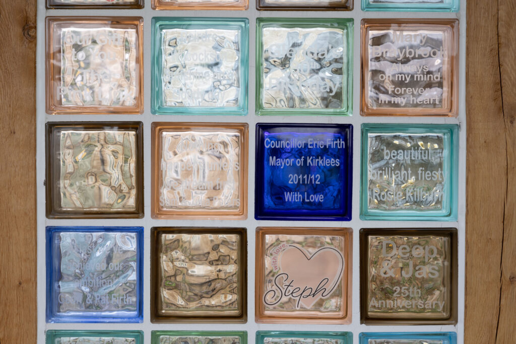 The memory wall at Russell House, showing a wall of coloured glass bricks, each having a message of remembrance on it dedicated to someone.