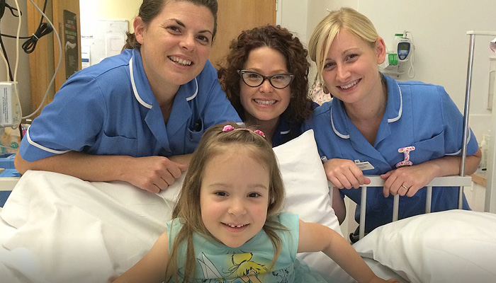 Three members of the care team staff around a bed with a little girl, all smiling.