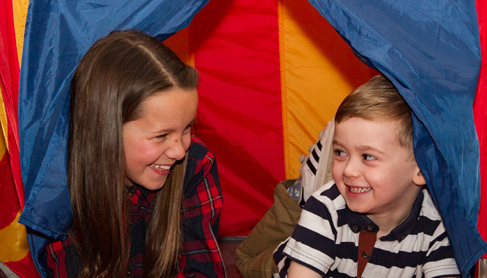 Two children, a boy and a girl, playing in an indoor tent smiling at each other.