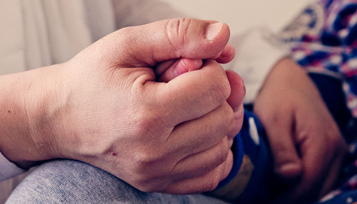 Close up picture of an adult hand holding a childs hand.
