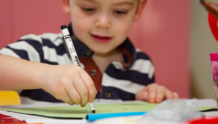 Close up picture of a child, a boy, drawing with a pen on a table.