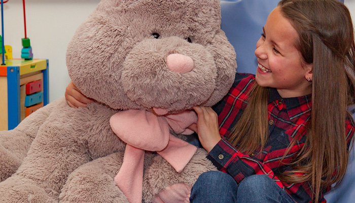 Young girl smiling and playing with a large teddy bear.